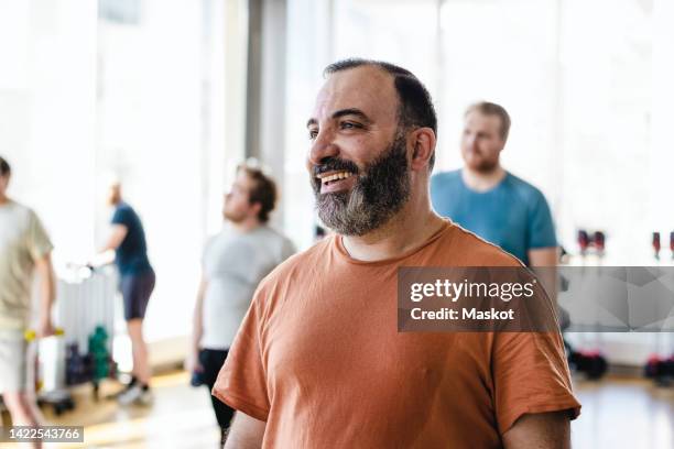 smiling man looking away with male friends in background at exercise class - arab group stockfoto's en -beelden