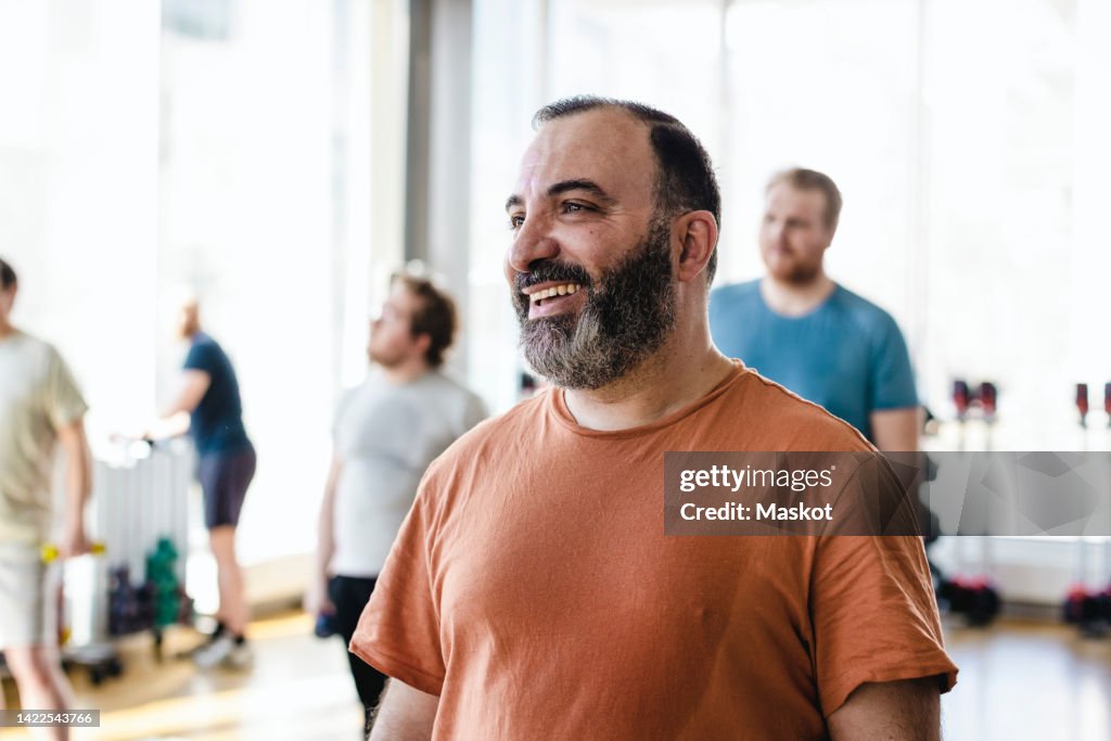 Smiling man looking away with male friends in background at exercise class