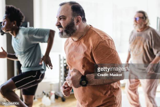 determined man doing jogging exercise with male friends in gym - 3 old men jogging stockfoto's en -beelden
