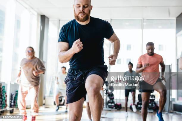 determined man practicing jogging with male friends during exercise class in gym - fitnesstraining stock-fotos und bilder