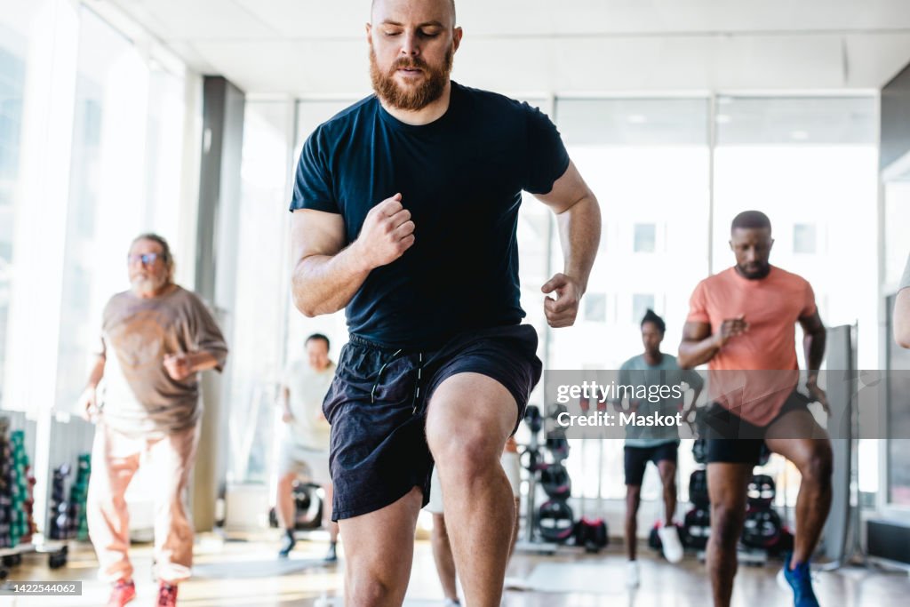 Determined man practicing jogging with male friends during exercise class in gym