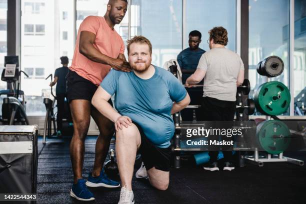 male fitness instructor assisting overweight man in exercise at gym - hombre gordo fotografías e imágenes de stock