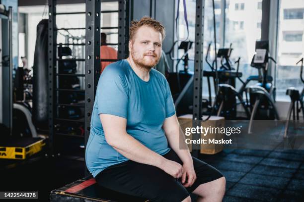 portrait of man sitting on bench in gym - hombre gordo fotografías e imágenes de stock