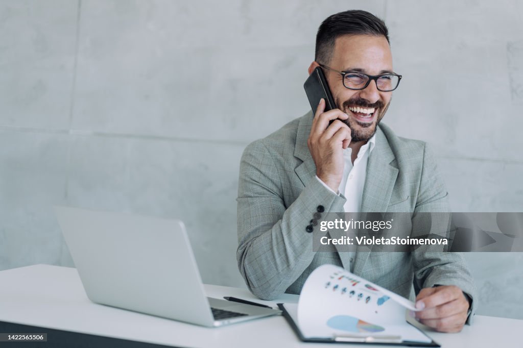 Businessman working on laptop and talking on cellphone.