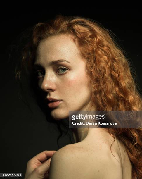 a portrait of a red-haired beautiful well-groomed young woman with curly hair on a black isolated background. the shirtless woman looks at the camera. she has freckles, wavy hair and hand on her shoulder. renaissance concept. - woman face art stock pictures, royalty-free photos & images