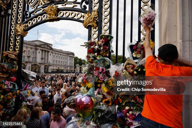 People pay their respect by placing flowers into the ironwork of a gate outside of Buckingham Palace following the death of Queen Elizabeth II on...