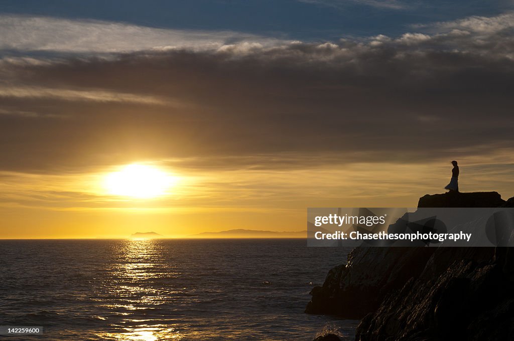 Silhouette of woman on cliffs at beach at sunset