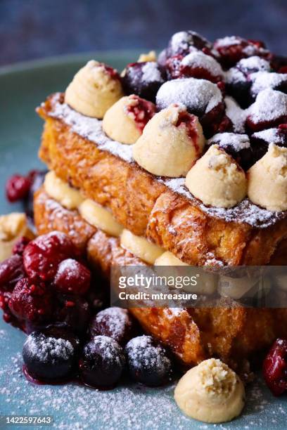 close-up image of blue plate with two slices of golden brioche french toast sandwiched together with piped chantilly cream (sweetened whipped cream with vanilla), topped with cream swirls and summer fruits (blackcurrants and cherries), focus on foreground - continental breakfast stock pictures, royalty-free photos & images