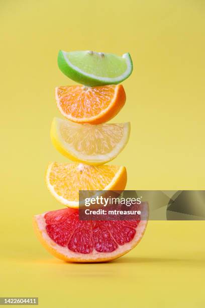 close-up image of alternating wedge slices of citrus fruit pile, lime, orange, lemon and pink grapefruit wedges, yellow background, focus on foreground - citrus fruit stock pictures, royalty-free photos & images