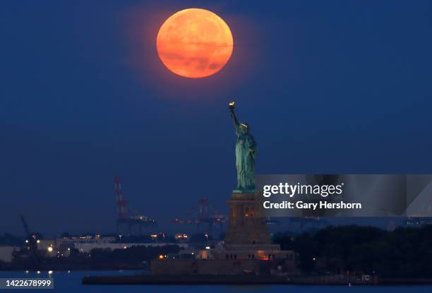 The full Harvest Moon sets behind the Statue of Liberty as the sun rises on September 10 in New York City.