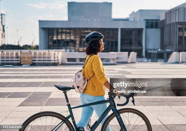 happy student walking with her bicycle to school in the city with a smile, happiness and reduce carbon footprint. eco friendly, commute and young girl cycling or riding a bike traveling to university - sports helmet stock pictures, royalty-free photos & images