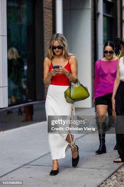 Guest wearing laced up white skirt, red top, green Prada bag outside Tibi on September 10, 2022 in New York City.