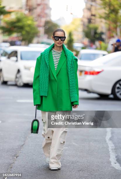 Guest wearing green oversized blazer, knit, striped shirt, creme white pants with side pockets outside Tibi on September 10, 2022 in New York City.