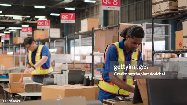 Two asian warehouse worker working checking package products in warehouse, logistic. While staff used laser barcode scanner on cardboard box, distribution center, placement in storage for shipping.
