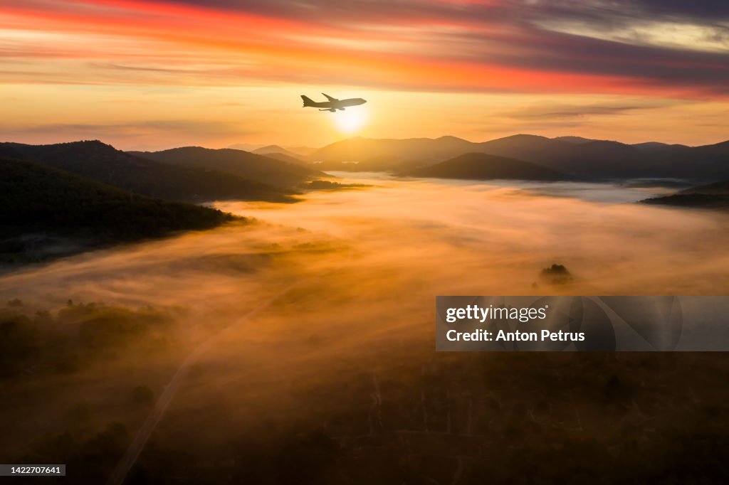 Airplane over misty mountains at dawn