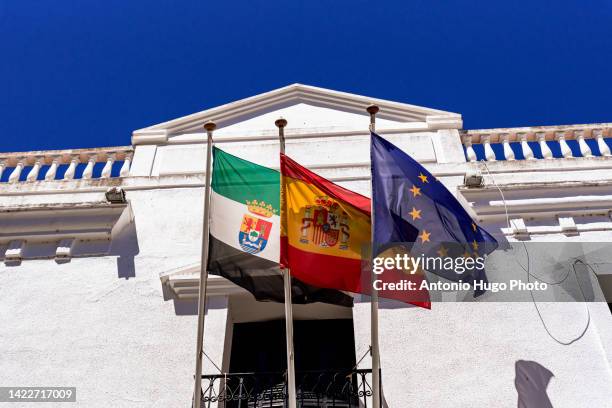 flags of spain, europe and extremadura hanging from a public building. - comunidad autónoma de extremadura fotografías e imágenes de stock
