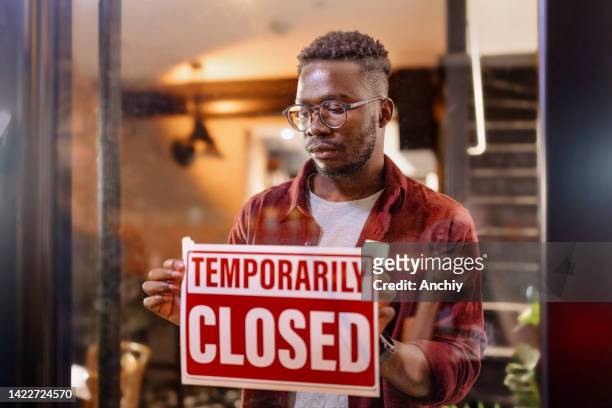 cropped shot of a man holding up a "temporarily closed" sign in his store - closing stockfoto's en -beelden