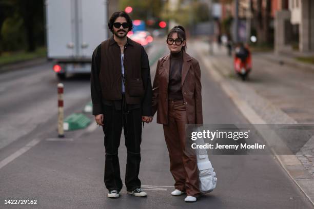 Enlil Isik is seen wearing black shades, necklaces, brown shirt, brown sweater vest, black denim jeans and black Converse Chuck Taylor sneaker;...