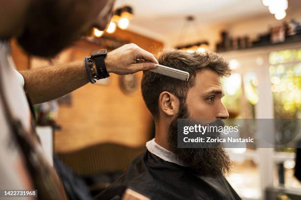 young barber making haircut to a bearded man using comb - beard trimming stock pictures, royalty-free photos & images