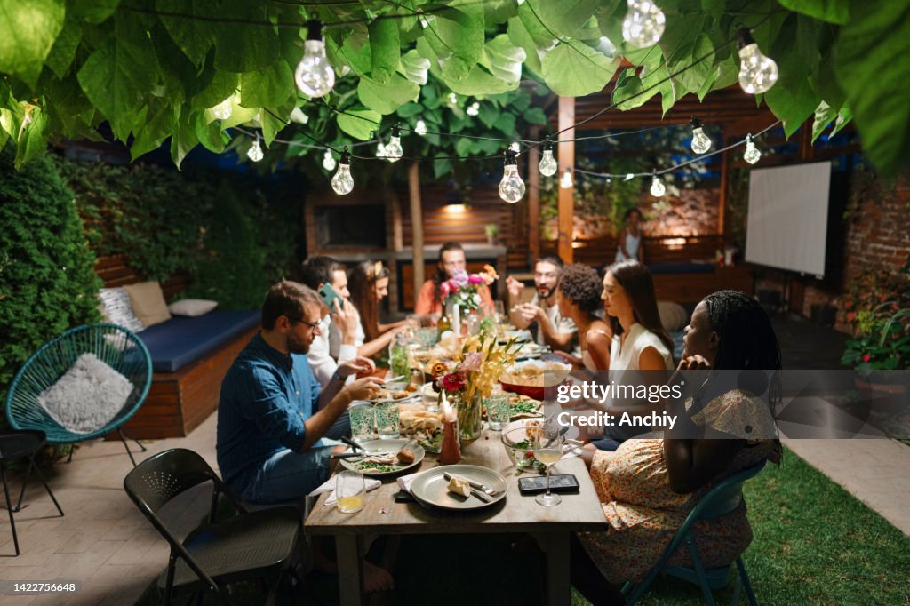 Family and some friends enjoying an outdoor meal in a courtyard together.