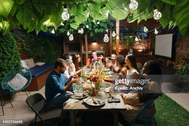 family and some friends enjoying an outdoor meal in a courtyard together. - family evening meal stock pictures, royalty-free photos & images