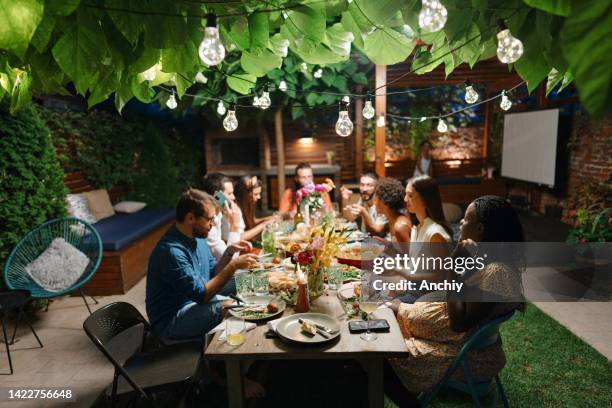família e alguns amigos desfrutando de uma refeição ao ar livre em um pátio juntos. - evening meal - fotografias e filmes do acervo