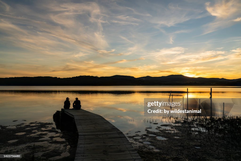 Two people watching the sunset on the Merimbula Boardwalk, Merimbula, NSW, Australia.
