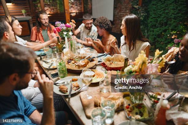 amigos alegres hablando mientras disfrutan de la cena en la mesa del comedor en la fiesta - cena con amigos fotografías e imágenes de stock