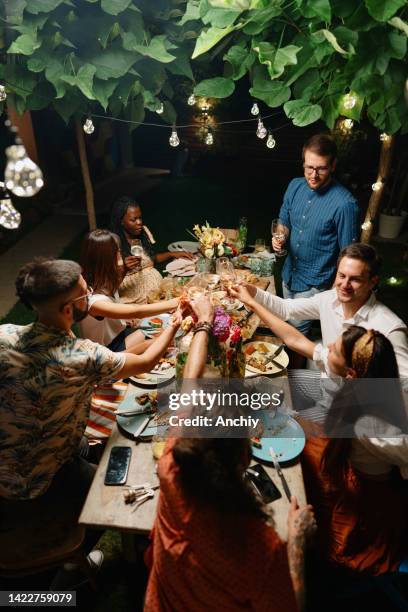 multi-ethnic friends toasting drinks at dinner table in yard - family dinner party stock pictures, royalty-free photos & images