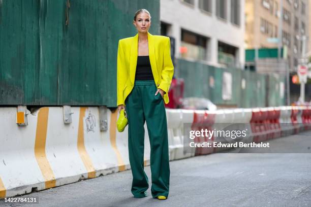 Leonie Hanne wears a gold First earring from Fendi, a yellow oversized blazer jacket, a black square neck top, a neon yellow braided leather handbag...