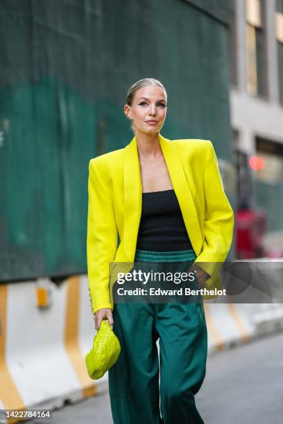 Leonie Hanne wears a gold First earring from Fendi, a yellow oversized blazer jacket, a black square neck top, a neon yellow braided leather handbag...