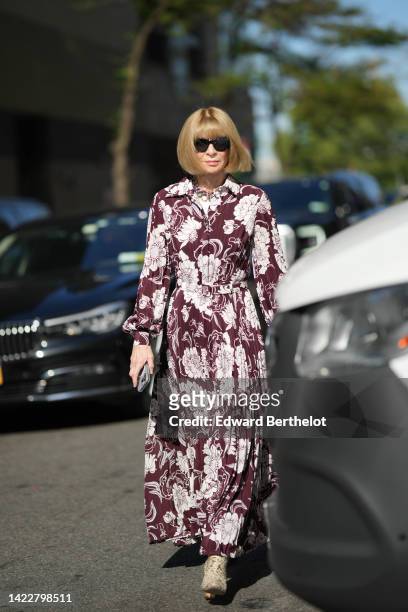 Anna Wintour wears black sunglasses, a burgundy with white flower print pattern shirt / puffy long sleeves / pleated long dress, beige and dark brown...