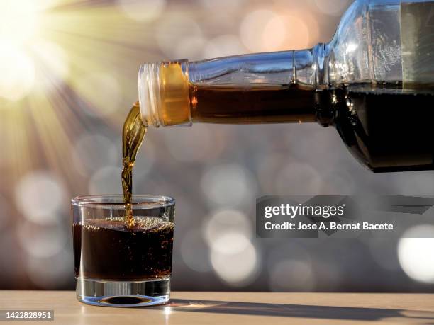 filling a shot glass with a liquor bottle lit by sunlight. - likör stock-fotos und bilder