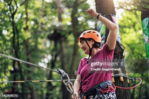 senior woman enjoying in the high ropes course - zip line stockfoto's en -beelden