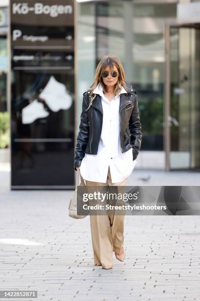 Gitta Banko wearing a white blouse by Jil Sander, beige pumps by Christian Louboutin, a black leather jacket by Loewe, beige pants by Loewe, a beige...