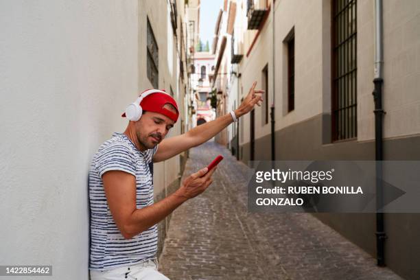 side view of white man wearing headphones dancing and listening to music with his mobile phone on city street. technology concept. - gonzalo caballero fotografías e imágenes de stock