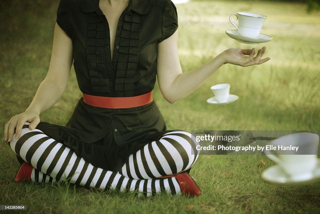 Woman sitting on grass with teacups in air