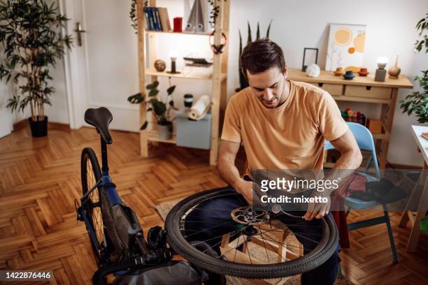 young casually clothed man inflating bicycle tire in his apartment - bicycle tire stock pictures, royalty-free photos & images
