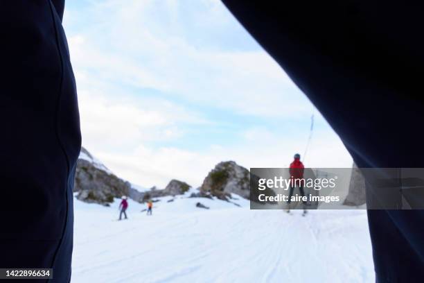 photo of the back of a person skiing in the snow taken through the legs of a person standing wearing jeans - ski pants stock-fotos und bilder