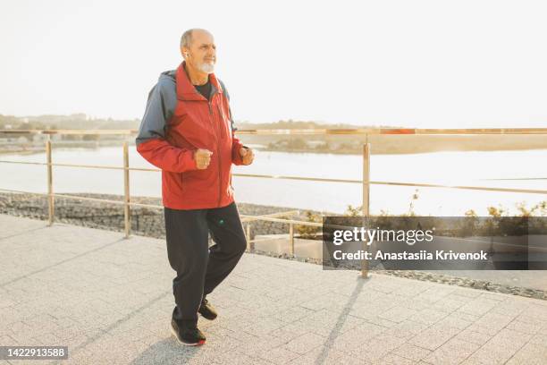 senior man in headphones running on park in sunshine morning. - first gray hair stock pictures, royalty-free photos & images