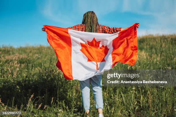 girl with a canadian flag walks across the field against the sky - canadians celebrate national day of independence 個照片及圖片檔