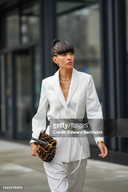 Katya Tolstova wears silver earrings, a silver and gold large chain necklace, a gold chain pendant necklace, a white with black small striped print...
