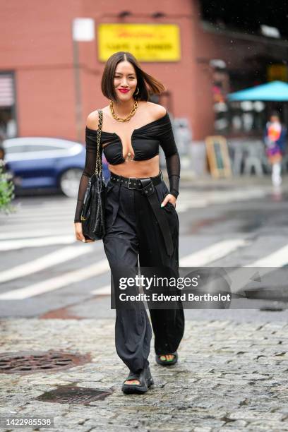 Tiffany Hsu wears a gold large chain necklace, a black V-neck / shoulder-off / long sleeves cropped top, a black shiny leather Chanel 22 large...
