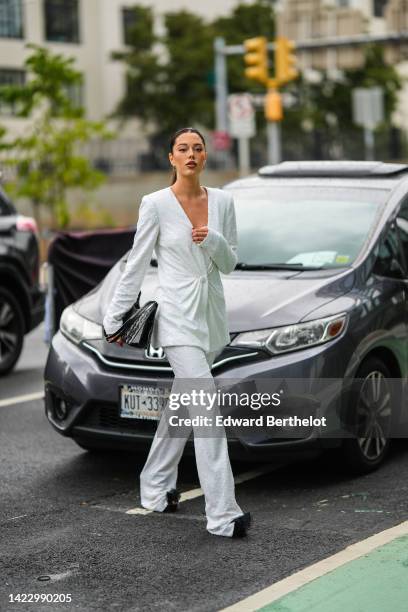 Guest wears gold earrings, a white embroidered sequined V-neck / shoulder-pads / blazer jacket, matching white sequined flared suit pants, a black...