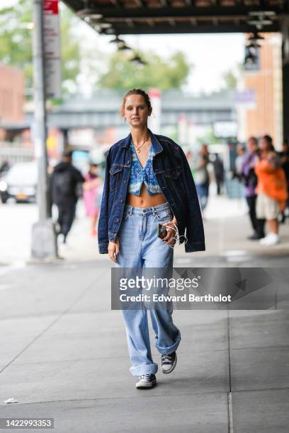 Guest wears gold earrings, a gold chain necklace, a blue with purple and green flower print pattern / buttoned / cropped gilet, a navy blue denim...