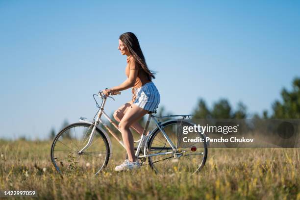 side view of young woman cycling on country track, smiling - girl bike stock pictures, royalty-free photos & images