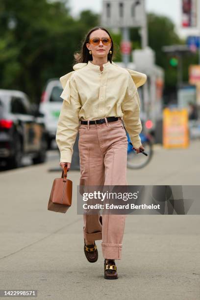 Guest wears orange sunglasses, gold earrings, a pale yellow linen / buttoned sleeves / ruffled shoulder shirt, a black shiny leather belt, pale pink...