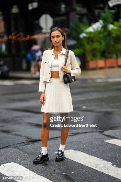 Guest wears a white shoulder-off / cropped top, a white latte buttoned jacket, a white latte embossed ribbed short skirt, a black shiny leather Boy...