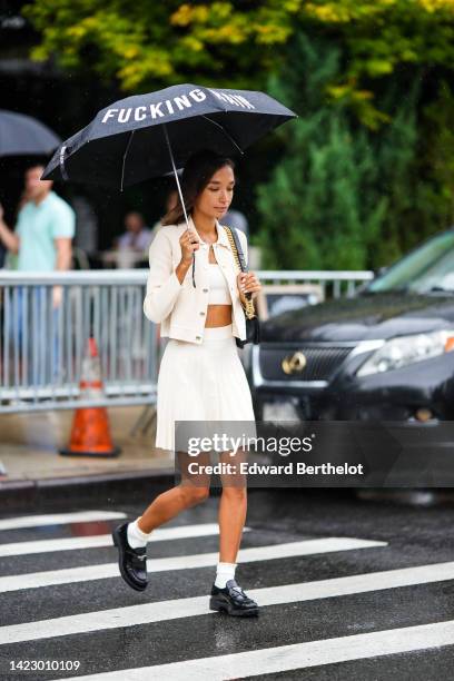 Guest wears a black umbrella, a white shoulder-off / cropped top, a white latte buttoned jacket, a white latte embossed ribbed short skirt, a black...