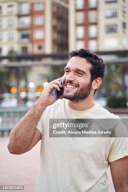 waist up front view of smiling young man talking on cell phone in the city. - shirt fotografías e imágenes de stock